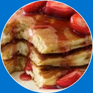 “Pancakes topped with cheesecake pieces and strawberries.”